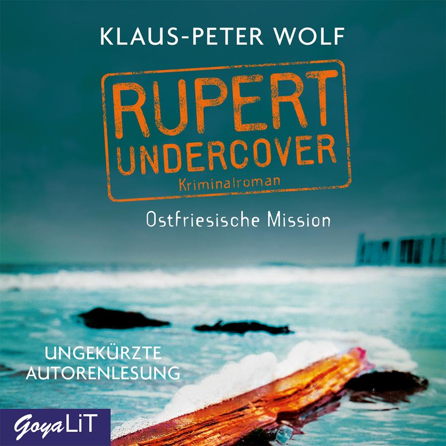 „Rupert Undercover – Kriminalroman: Ostfriesische Mission“ von Klaus-Peter Wolf: Cover mit einem Strand unter bewölktem Himmel. Oben stehen der Name „Klaus-Peter Wolf“, der Reihenname „Rupert Undercover“, der Zusatz „Kriminalroman“ sowie der Titel „Ostfriesische Mission“. Links unten steht „Ungekürzte Autorenlesung“. Im Vordergrund liegt ein angespülter Baumstamm im flachen Wasser. Im Hintergrund sind Brandung, mehrere dunkle Felsen sowie rechts Buhnen im Meer zu sehen. Unten links befindet sich das Logo „GoyaLiT“.